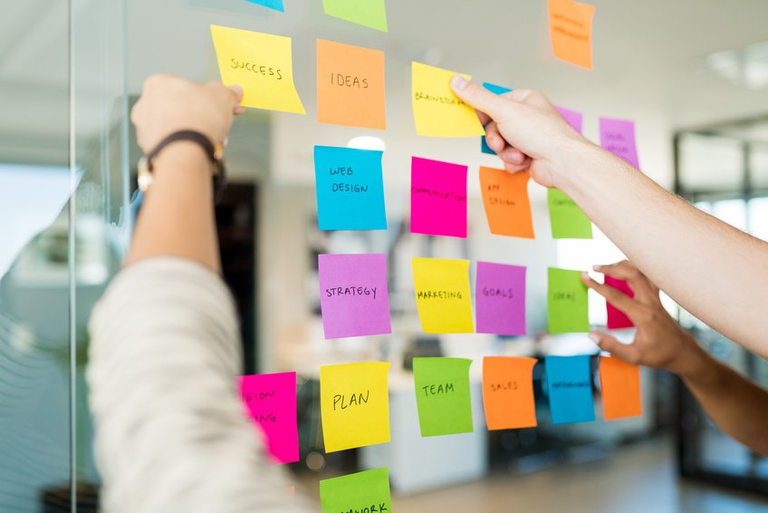 Hands arranging colourful planning notes on a glass wall