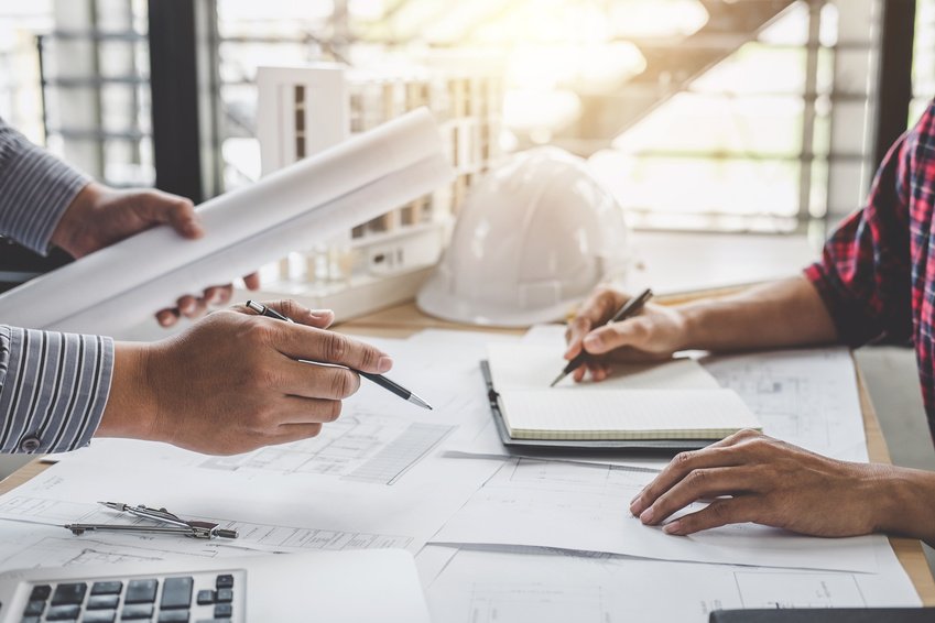 Engineering professionals reviewing blueprints beside a hard hat